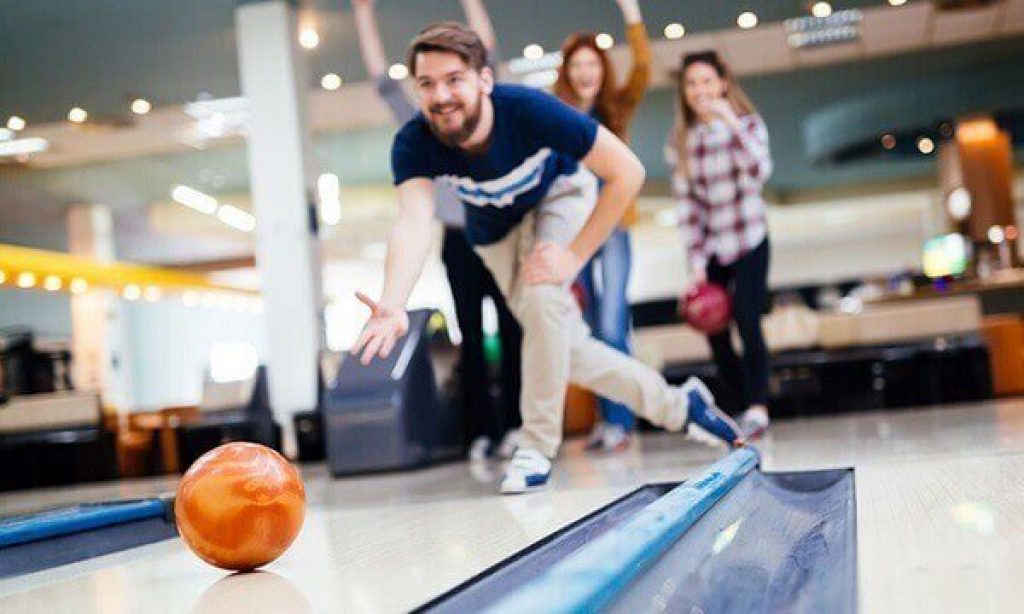 A young male throwing a bowling ball while three of his friends are watching and supporting him - Pyramid Antidote Bowling Ball Review